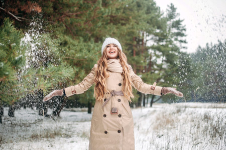 A girl in a pine forest throws snow with her hands and rejoices. Concept - New Year, Christmas,...