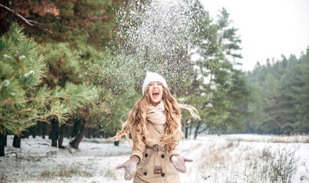 A girl in a pine forest throws snow with her hands and rejoices. Concept - New Year, Christmas, postcard, banner. Place for textの写真素材