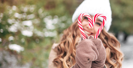 Close-up of women's hands holding sweets in the form of hearts. Sweets in the hands of a woman on the background of a green Christmas tree. Small depth of field with emphasis on handsの写真素材