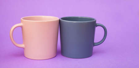 Two cups pink and gray color for coffee, stand on a purple background. A place for text. Banner. coffee day. Valentine's Day. Close up cups. Minimalism with coffee. Breakfastの写真素材