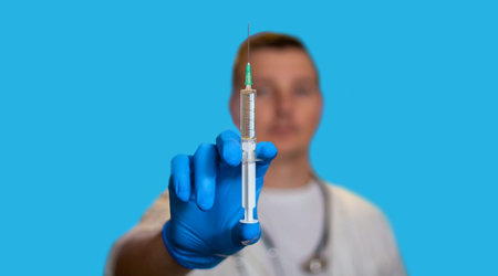 Close-up of the syringe. The doctor holds a syringe in his hands. A young doctor stands on a blue background. A place for text. Medicineの写真素材