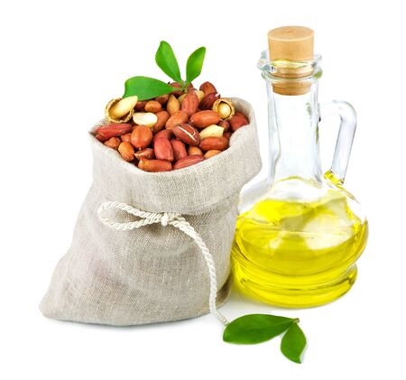 Macro view of peanut in flax sack and glass bottle of oil with leaves isolated on white backgroundの写真素材