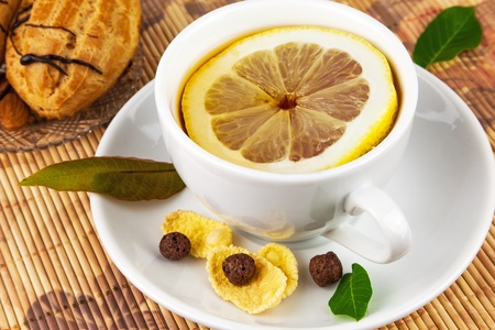 Cup of tea with slice cut of lemon on plate, cakes and leaves on the matの写真素材