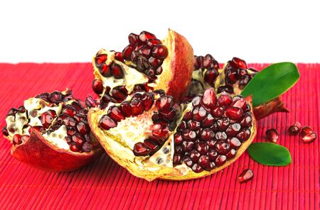 Grains of pomegranate with green leaves on red mat isolated on white backgroundの写真素材