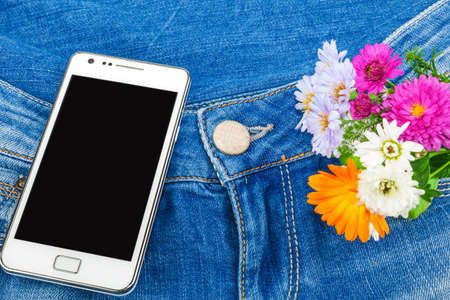 White mobile phone in pocket of blue jeans with flowersの写真素材