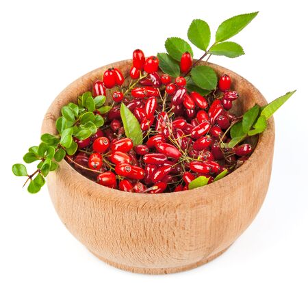 Branches of barberries in wooden bowl with green leaves isolated on white backgroundの写真素材