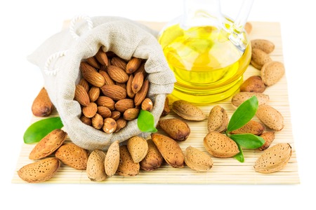 Almonds in the sack, almond oil and green leaves on mat isolated on white backgroundの写真素材