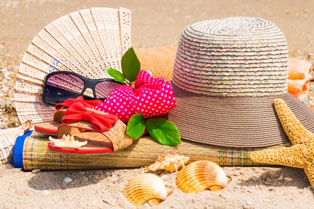 Hat, flip flops, glasses, green leaves on mat on beachの写真素材