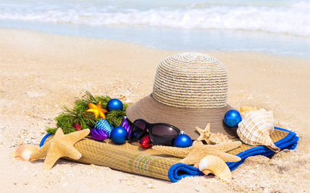 Christmas balls, hat, shells, sunglasses on the mat on the beach