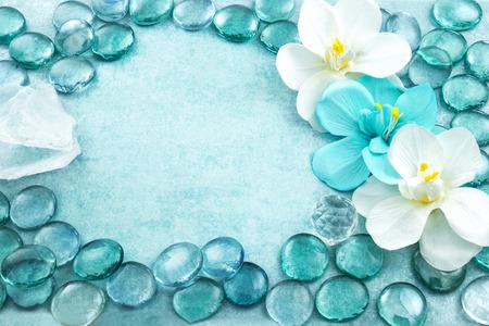 Macro view of blue glass drops with white flowers orchid and bar of sea salt, aqua backgroundの写真素材