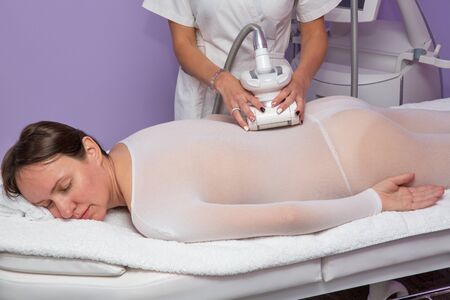 Woman in the white special suit having anti cellulite massage with apparatusの写真素材