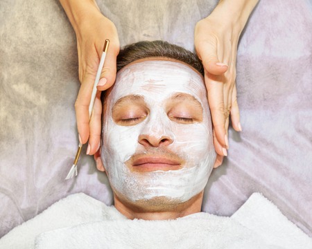 Face of laying man with cream mask, hands of beautician with brush, beauty, spaの写真素材