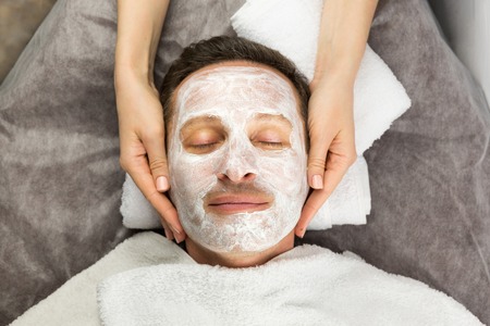 Face of man with cream mask and hands of professional cosmetologist, beauty, spaの写真素材