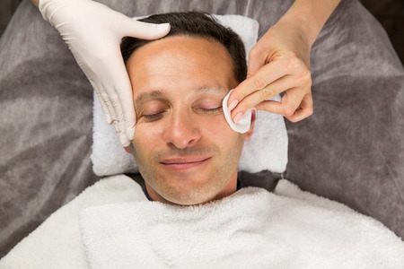 Male face, hands of professional beautician with gloves and white cotton spongesの写真素材