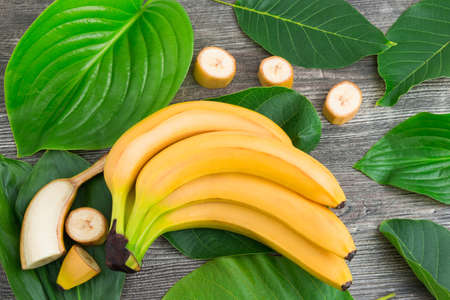 Macro view of bunch of fresh raw organic yellow bananas with slices and green leaves on wooden backgroundの写真素材
