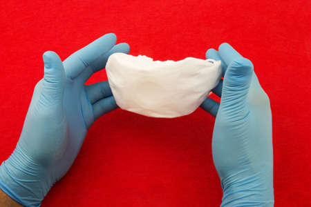 Male hands with blue rubber gloves and hold white medical mask on red backgroundの写真素材