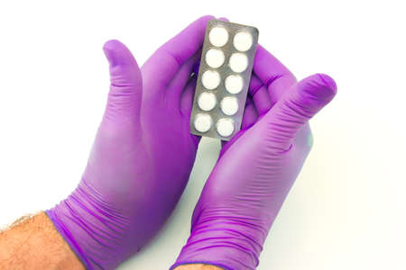 Male hand with lilac rubber glove hold tablets in packaging on white backgroundの写真素材