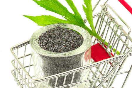 Macro view of poppy seeds with green leaves in glass bowl in shopping trolley on white backgroundの写真素材