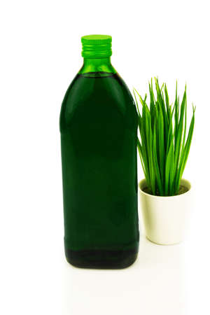 Green healthy superfood concept. Glass bottle of chlorophyll drink with fresh grass, wheat in bowl. Isolated on white background.の写真素材