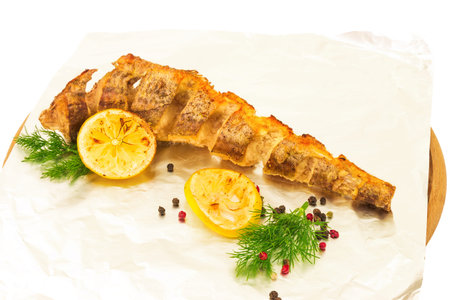 Macro view of baked tasty fish hake, pollock on foil with lemon, pepper mixture and dill on wooden...