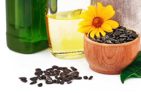Sunflower oil in glass bottles, sunflower seeds in sack and rustic wooden bowl with fresh flower and leaves on white backgroundの写真素材