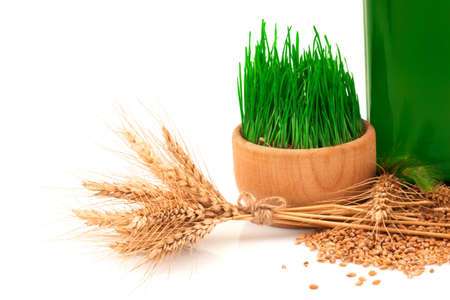 Macro view of glass green bottle with oil, sprouts of wheat in wooden bowl and ears of wheat with burlap tied isolated on white backgroundの写真素材