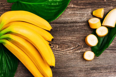 Macro view of bunch of fresh raw organic yellow bananas with slices and green leaves on wooden backgroundの写真素材