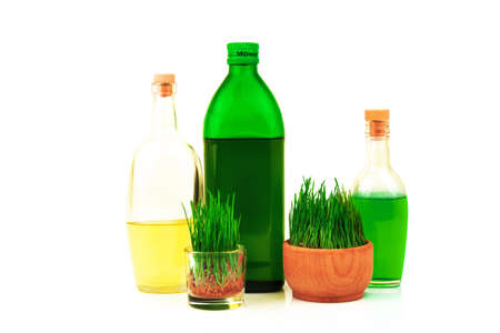 Glass bottles with oil and juice and fresh sprouts of wheat in wooden bowl isolated on white backgroundの写真素材