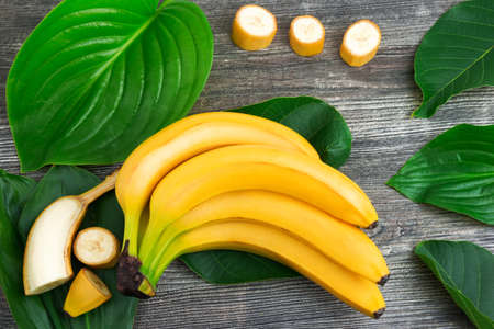 Macro view of bunch of fresh raw organic yellow bananas with slices and green leaves on wooden backgroundの写真素材