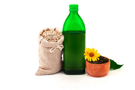 Sunflower oil in glass bottle, sunflower seeds in sack and rustic wooden bowl with fresh flower and leaves on white backgroundの写真素材