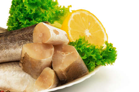 Macro view of raw slices of fish hake, pollock on the plate with lemon and leaves of salad lettuce isolated on white background.の写真素材