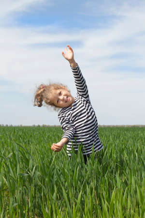 Cute curly-haired baby girl on a clear day on a green grass field. Walking and playing in the fresh air, freedom, joy. happy childhood. A summer day. Caring for nature and environmental friendlinessの写真素材