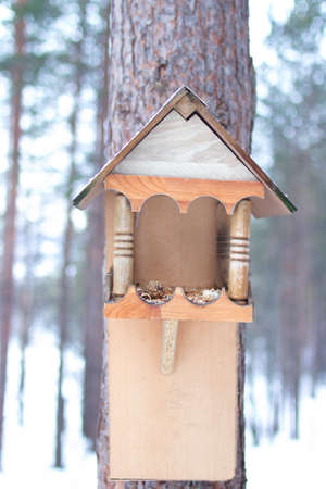 Birdhouse on a tree, close-up, handmade. Painted wooden bird feeder on a tree trunk in winter. vertical photo.の写真素材