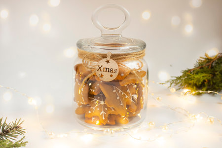 christmas composition. A jar of Christmas ginger cookies on a light background with garlands and bokeh. Template for a postcard, calendar. Edible handmade souvenirs. The concept of New Year's gifts. copy spaceの写真素材