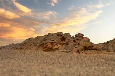 A beautiful mountain with holes of caves on the background of a colorful sky. Steppe landscape with dry grass, mountain and sky. horizontal photoの写真素材