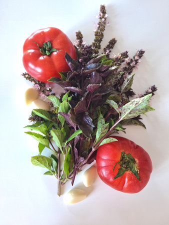 Juicy ripe red tomatoes, fresh basil and garlic cloves on a light background. Flatly. Fresh natural ingredients for cooking. A concept for cooking blogs, recipes, magazine covers, and food packagingの写真素材