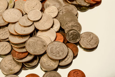 Different American coins lie in a heap on the reflecting surface.
