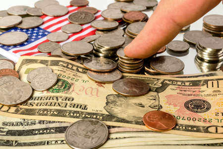 Different American coins and banknotes and the American flag lie on the reflecting surface. And the human finger on top.の写真素材