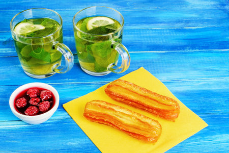 Two transparent cups with mint and lemon on a wooden blue background. Two cakes on a yellow paper...