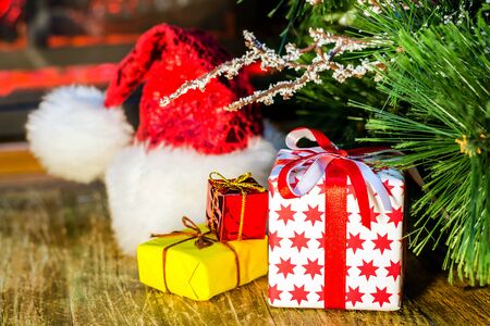 Santa hat and Christmas gift lie on the wooden surface near the fireplace. Selective focus. Blurred background. Horisontal shot.の写真素材