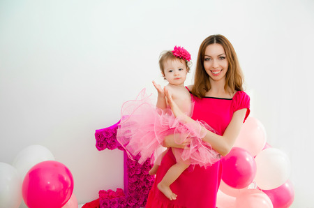 mother holding a baby in her arms. Little girl in a pink skirt. On a light background.First Birthday girl.の写真素材