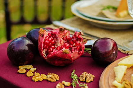 Sliced Pomegranate with plums on a maroon table.の写真素材