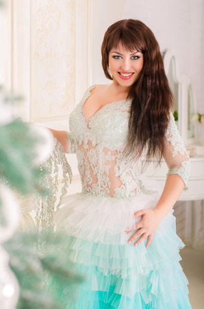 Beautiful girl smiling in mint wedding dress, standing by the fireplace near a Christmas tree.の写真素材