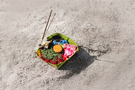 Traditional balinese offerings to gods in Bali with flowers and aromatic sticks. Hindu offering on sand with pink flower and biscuits in Bali, Indonesia, Asiaの写真素材