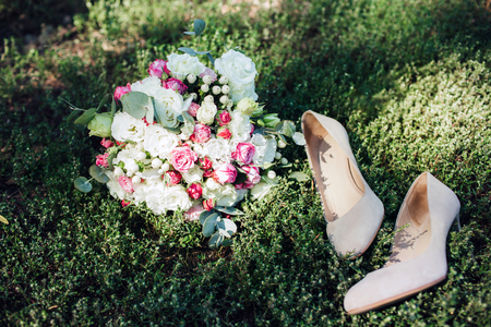 Wedding accessories: shoes and bride's bouquet. Beautiful wedding bouquet of small roses. Beige shoes on a background of a beautiful background of greenery.の写真素材