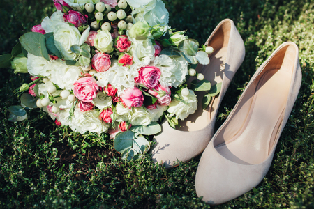 Wedding accessories: shoes and bride's bouquet. Beautiful wedding bouquet of small roses. Beige shoes on a background of a beautiful background of greenery.の写真素材