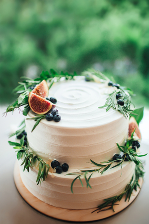 Wedding white cake with figs and raspberries. Rustic wedding cake decorated with figs, blueberries and greenery rosemary.の写真素材