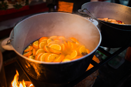 Hot gluhwein or mulled wine in a cauldron at fair, local treat, warm and spicy. A hot wholesome traditional citrus drink on fair. Vitamins in the winter festival. Black pot to cook the mulled wine in the country festival in europe.Christmas market.の写真素材