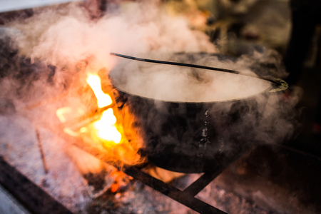 Hot gluhwein or mulled wine in a cauldron at fair, local treat, warm and spicy. A hot wholesome traditional citrus drink on fair. Vitamins in the winter festival. Black pot to cook the mulled wine in the country festival in europe.Christmas market.の写真素材