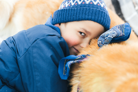 Christmas happy child boy running playing with Akita-Inu dog on white snow in winter day. A happy boy hugging his beloved dog, playing in the snow-covered forest.の写真素材